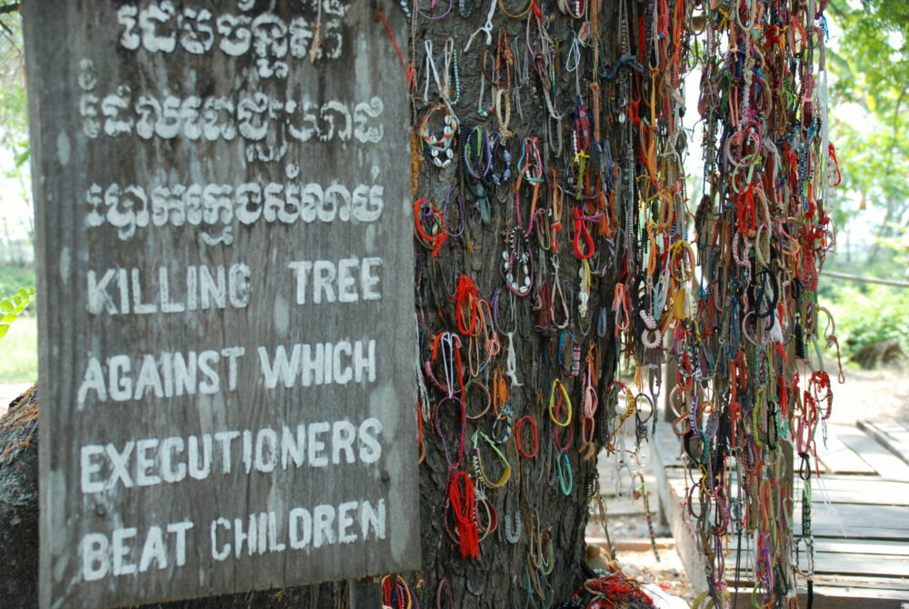 Panneau commémoratif et tronc du Killing Tree recouvert de bracelets colorés au mémorial de Choeung Ek.