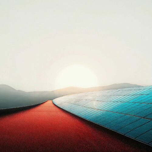 Un chemin rouge longe une surface de panneaux solaires bleus au lever du soleil dans un paysage montagneux.