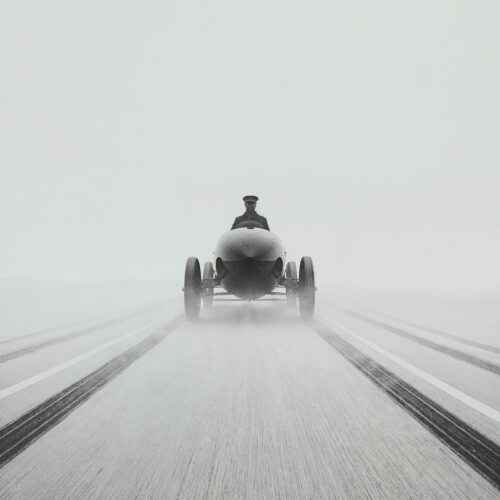 Voiture de course vintage roulant de face sur une piste couverte de brouillard.