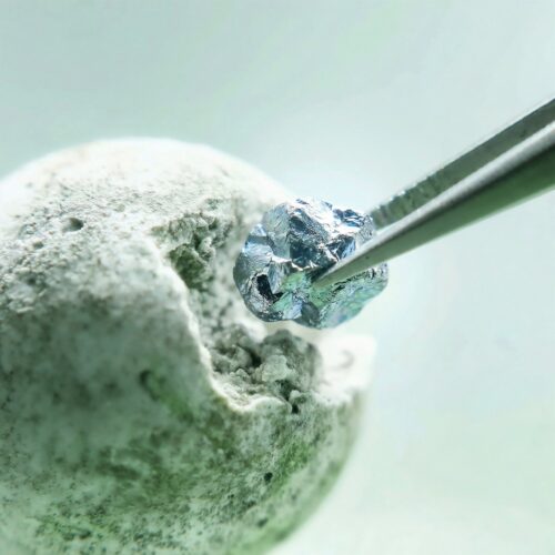 Pince de précision extractant un petit diamant brut bleu encastré dans une roche.