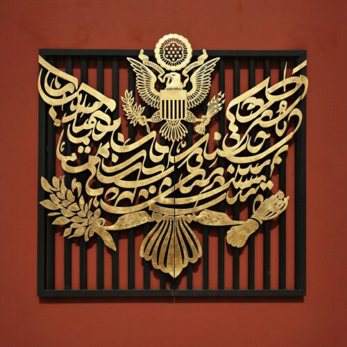 Sceau des États-Unis retravaillé avec de la calligraphie arabe dorée sur fond rouge.