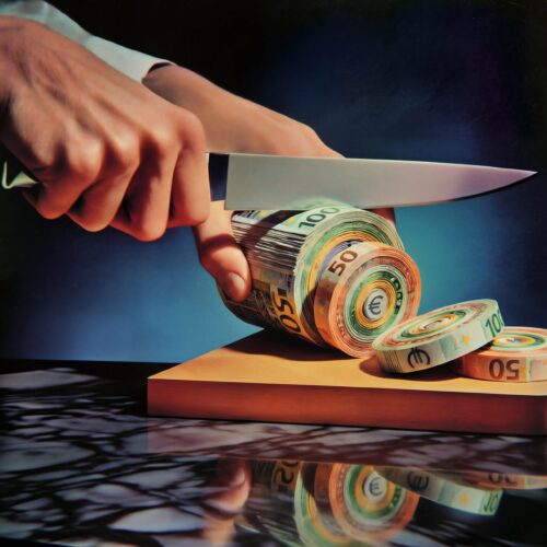 Mains coupant un rouleau de billets de banque avec un couteau de cuisine sur une planche à découper.