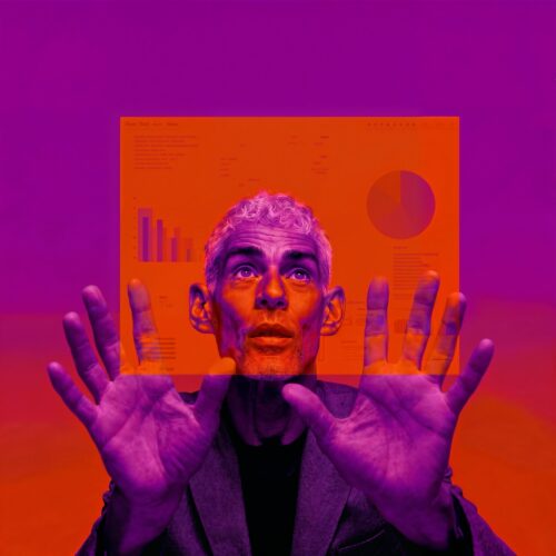 Homme levant les mains devant une interface numérique affichant des graphiques sous un éclairage violet et orange.