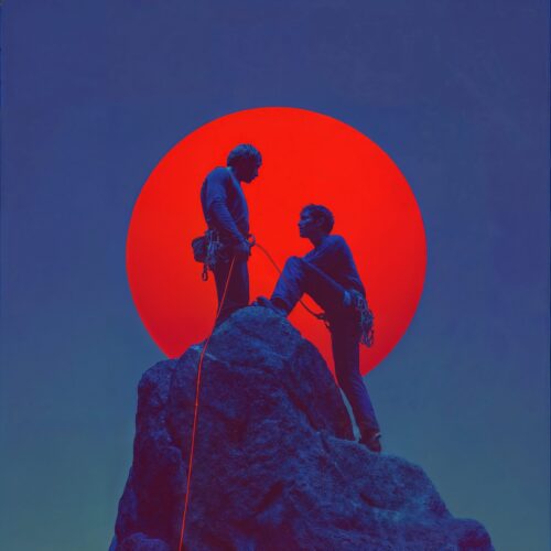 Deux grimpeurs au sommet d'un rocher devant un grand soleil rouge.