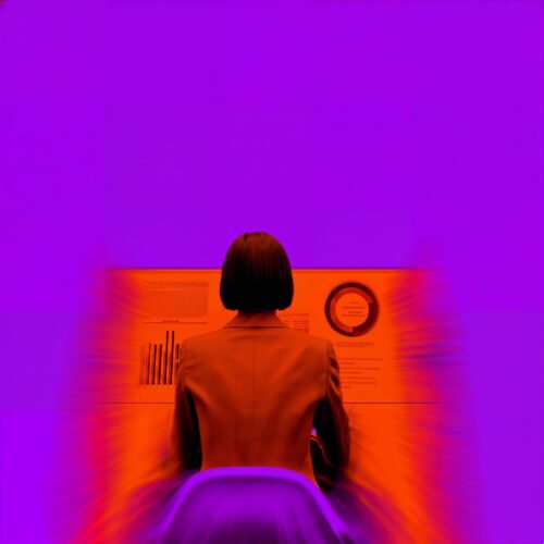 Vue de dos de Céleste assise devant un panneau lumineux affichant des graphiques dans un décor violet.