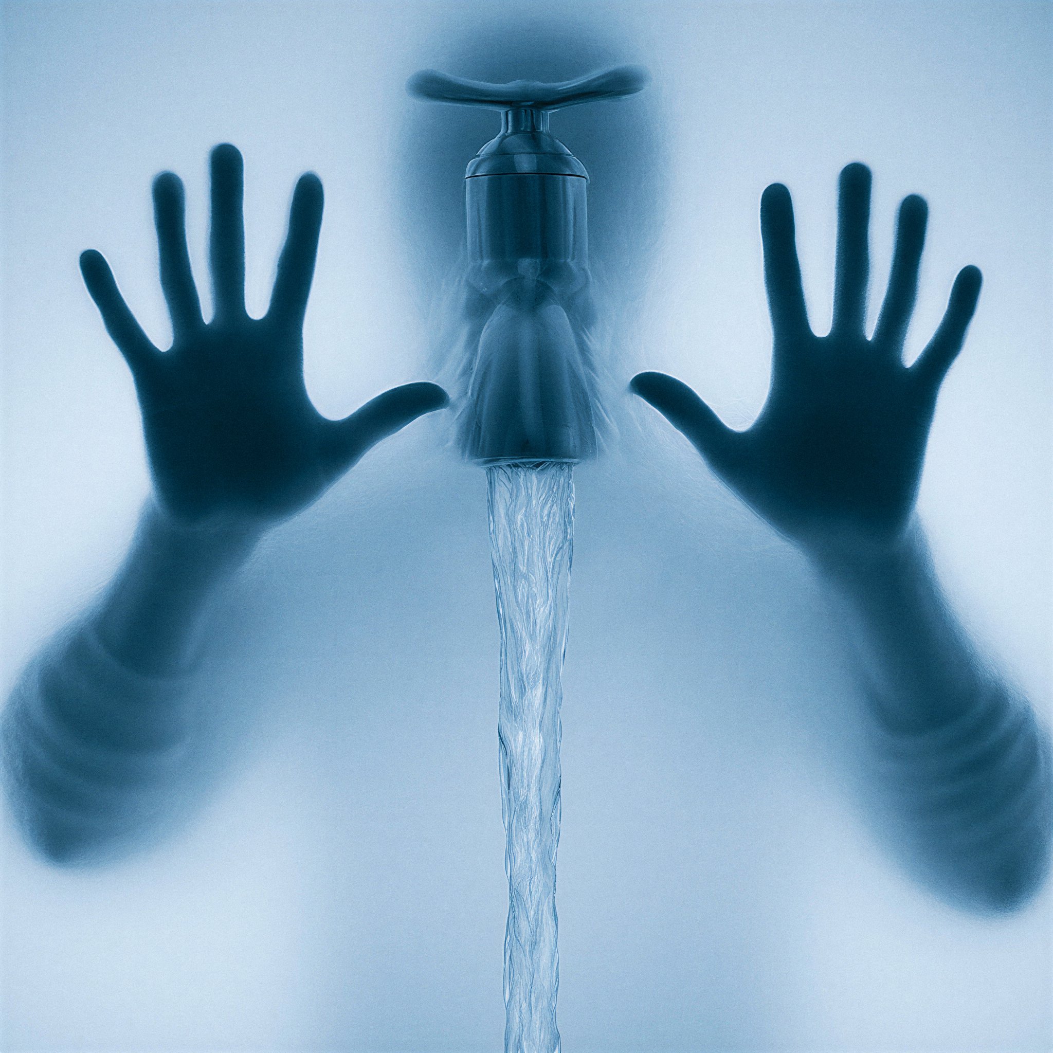 Silhouette floue derrière du verre dépoli avec des mains plaquées et un robinet coulant au centre.