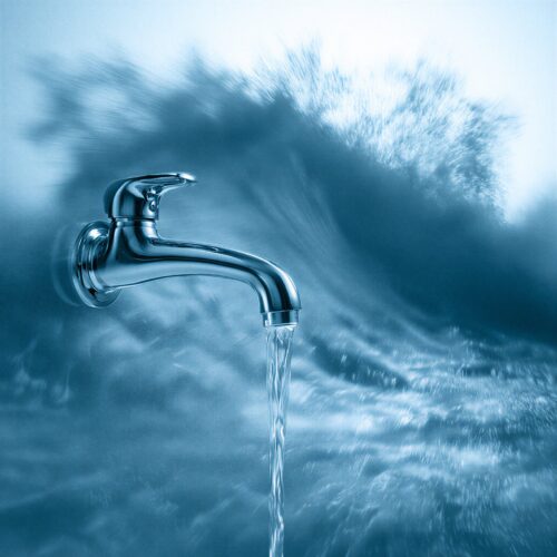 Robinet en métal chromé laissant couler un filet d'eau claire sur un fond bleu dynamique d'écume.