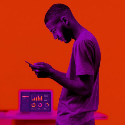 Profil d'un homme consultant son téléphone portable à côté d'un ordinateur affichant un tableau de bord analytique.