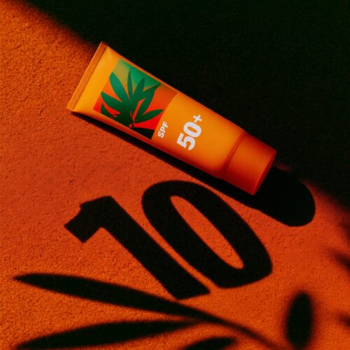 Un tube de crème solaire SPF 50+ posé sur une surface orange éclairée par le soleil avec l'ombre du chiffre 100