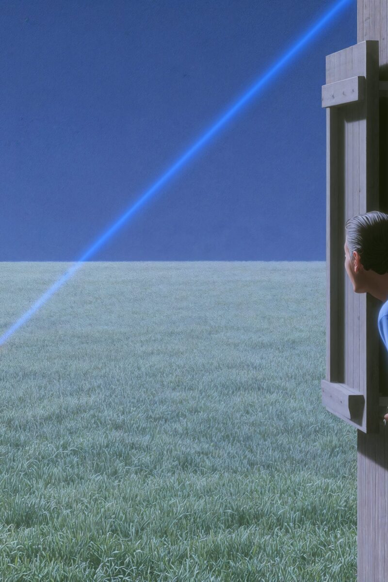 Un homme regarde par une fenêtre en bois un rayon lumineux bleu traverser un grand champ d'herbe.
