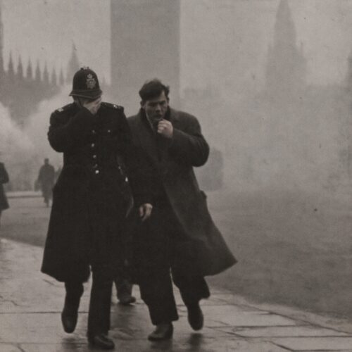Un policier londonien et un passant se couvrent le visage en marchant dans un épais brouillard de pollution.