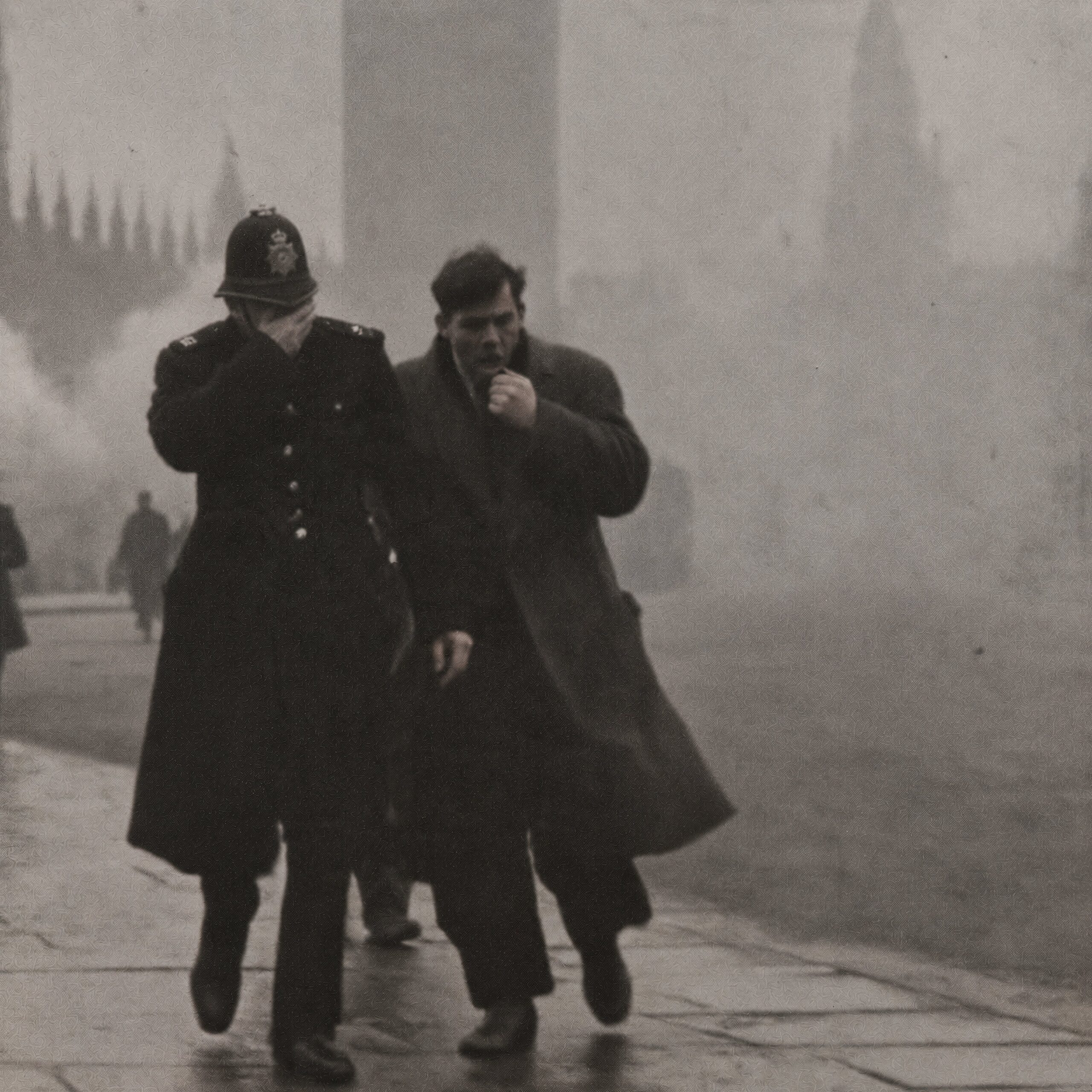Un policier londonien et un passant se couvrent le visage en marchant dans un épais brouillard de pollution.