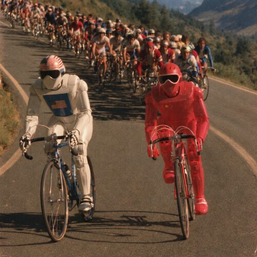 Deux cyclistes en armure futuriste aux couleurs des États-Unis et de la Chine mènent un peloton sur une route de montagne.