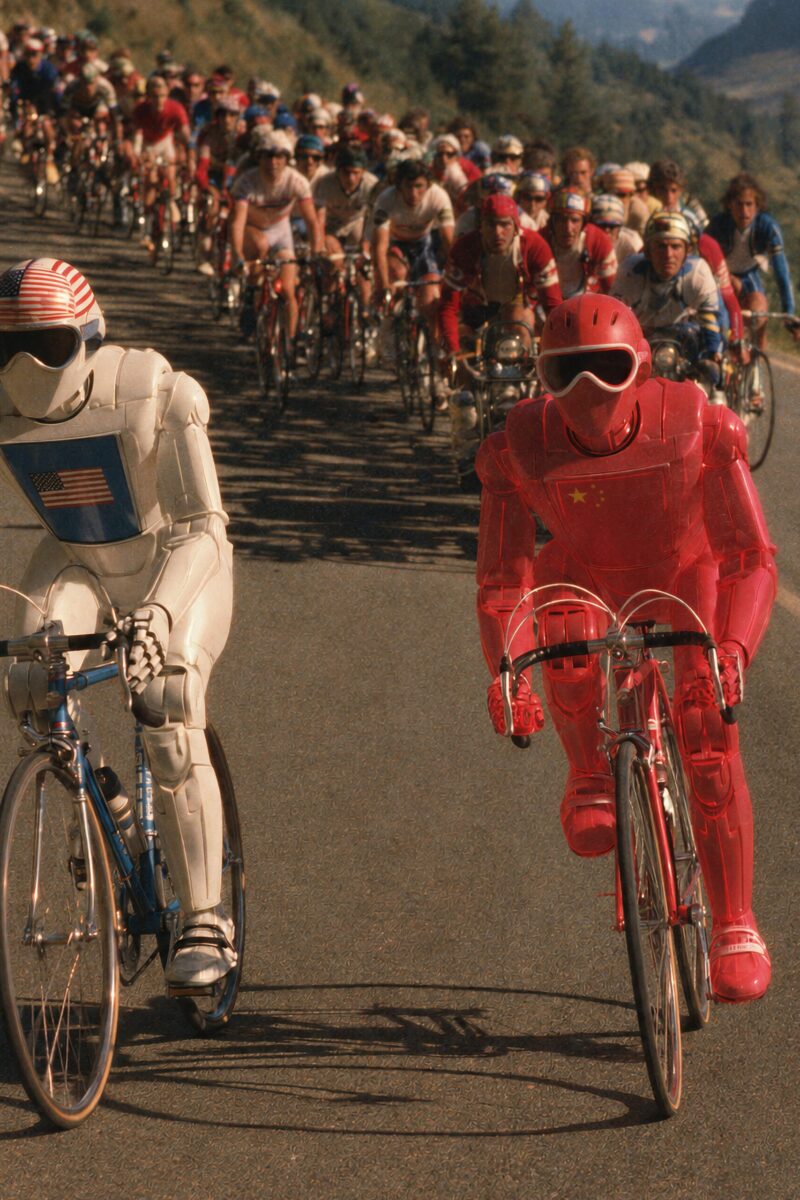 Course cycliste futuriste avec robots et peloton Deux cyclistes en armure futuriste aux couleurs des États-Unis et de la Chine mènent un peloton sur une route de montagne.