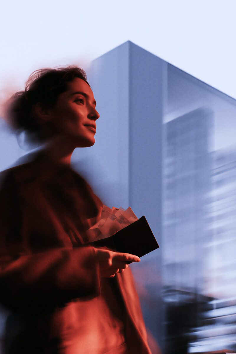 Une femme marchant dans la ville avec un effet de flou de mouvement, tenant un portefeuille ouvert.